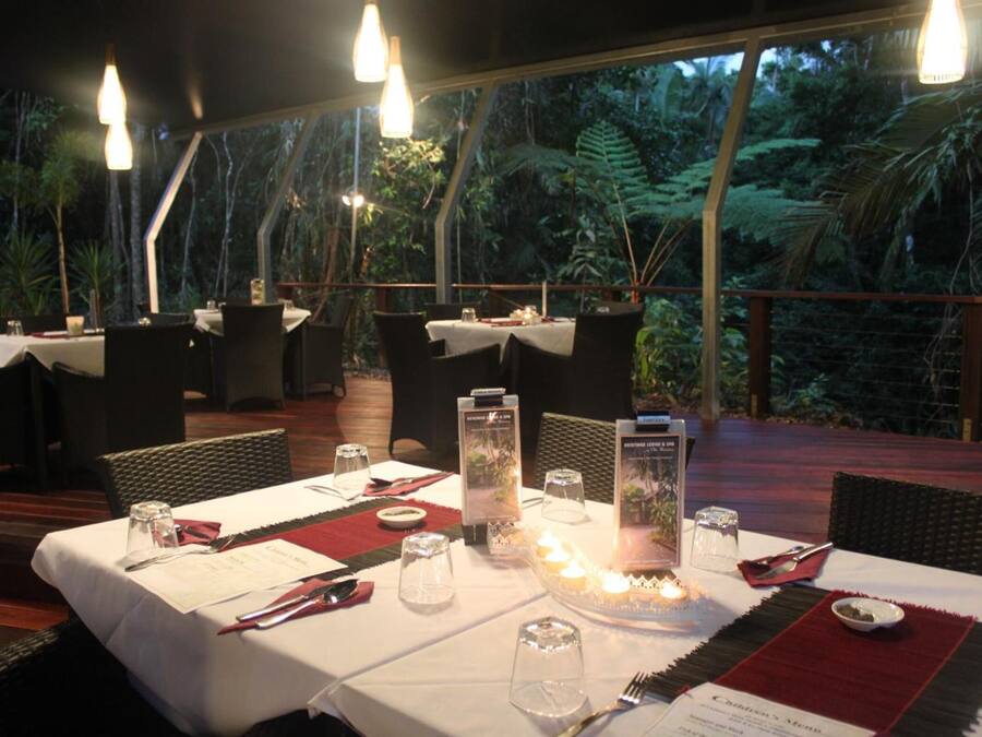 An outdoor dining area with tables set for two, surrounded by lush greenery.