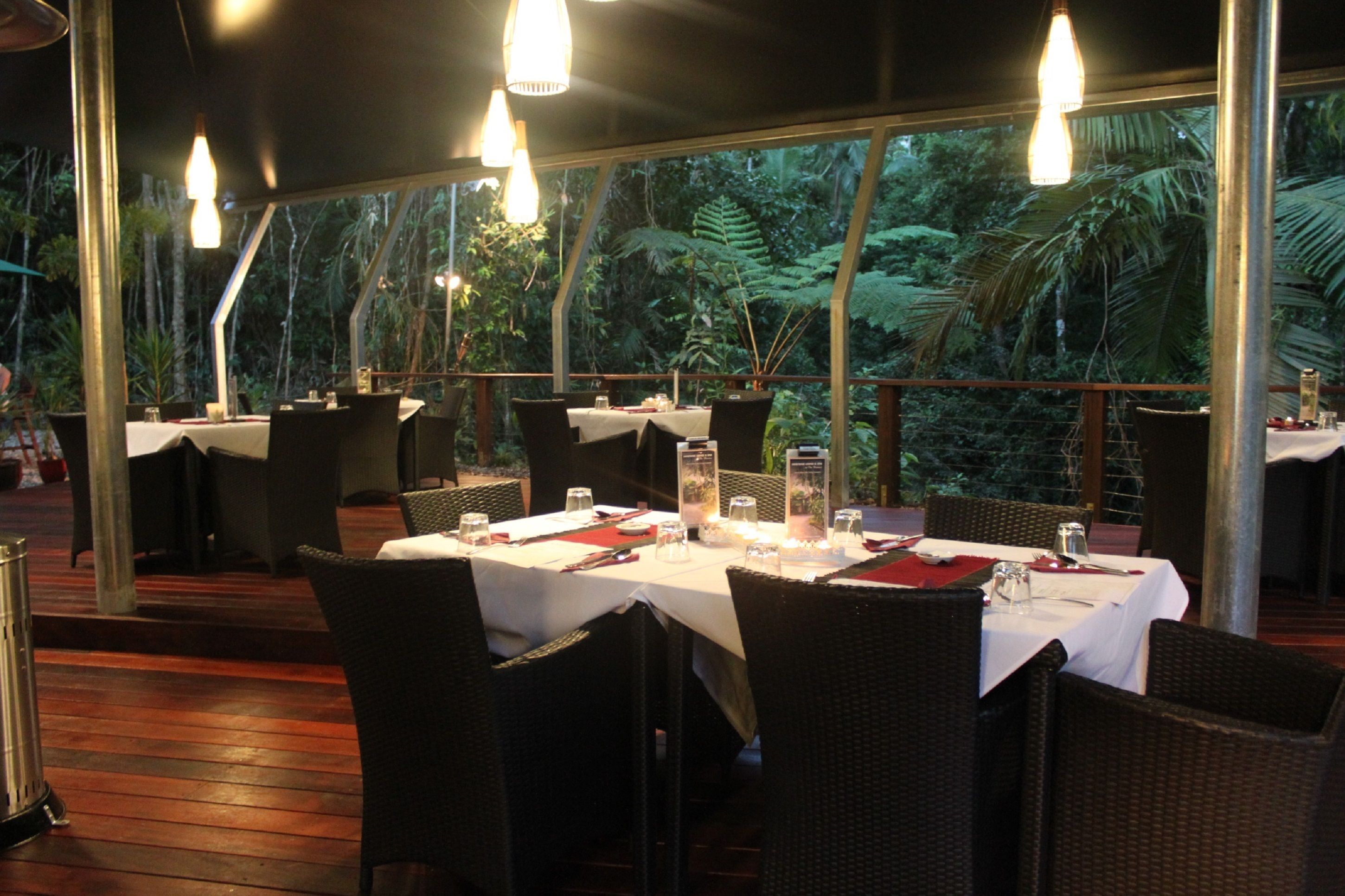 An outdoor dining area with tables set for two, surrounded by wicker chairs and a wooden deck.