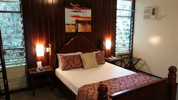A neatly made bed with a floral bedspread, two bedside lamps, a nightstand with a lamp, and a window with blinds.