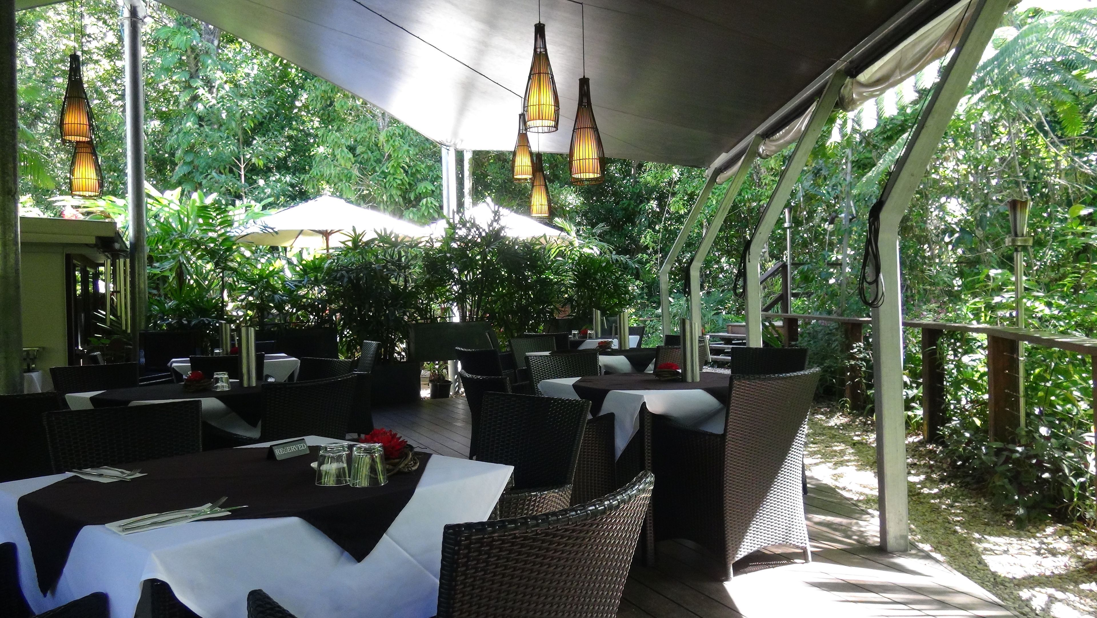An outdoor dining area with tables and chairs, surrounded by greenery.