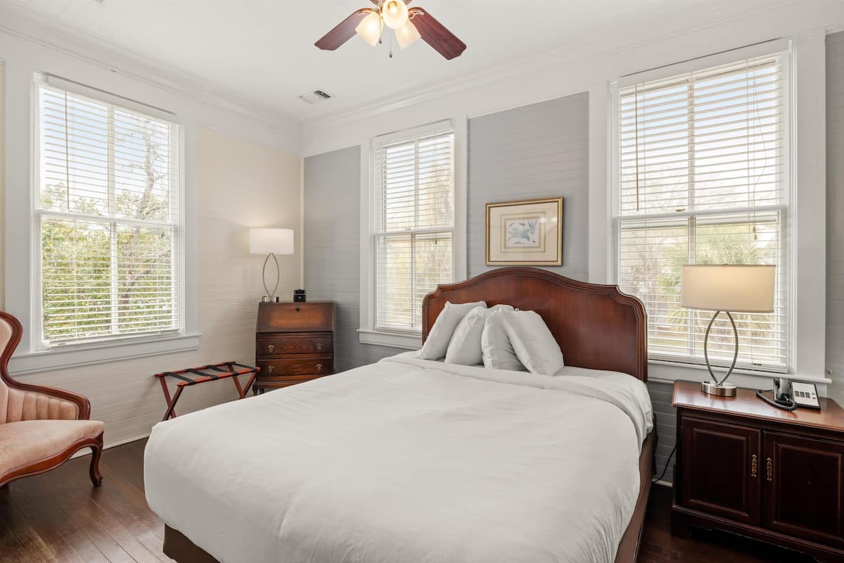 A bedroom with a large bed, wooden headboard, a dresser, a nightstand, a lamp, and a ceiling fan.