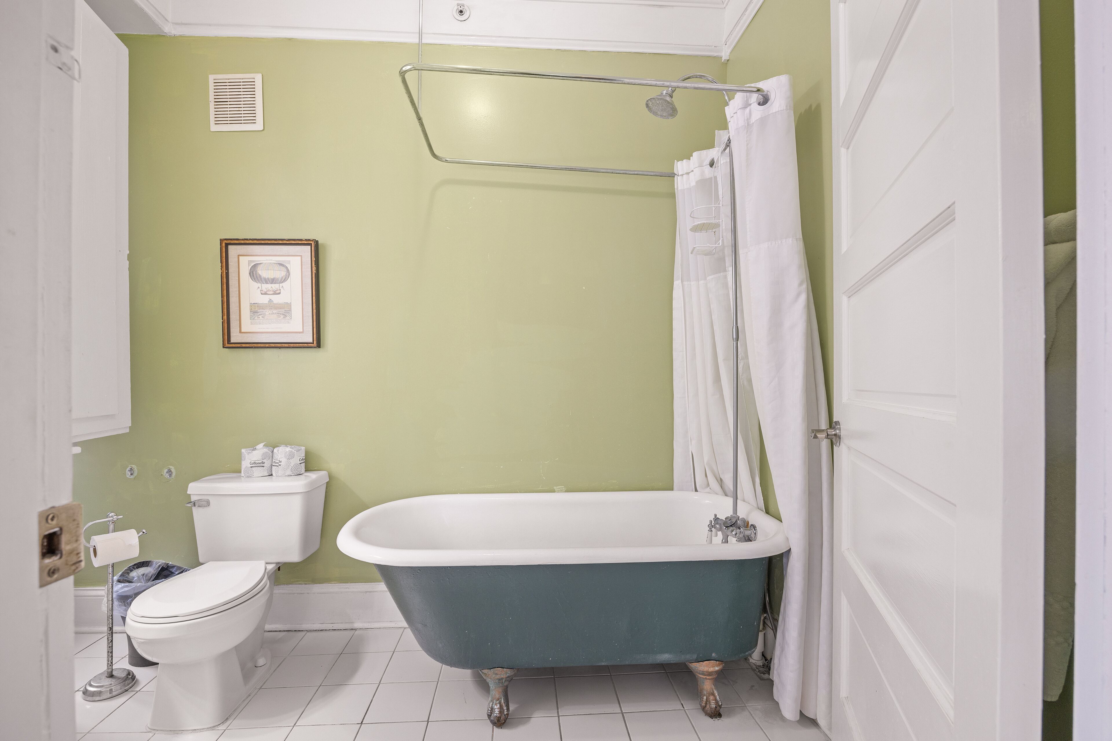 A bathroom with a white toilet, a blue clawfoot bathtub, and a white sink.
