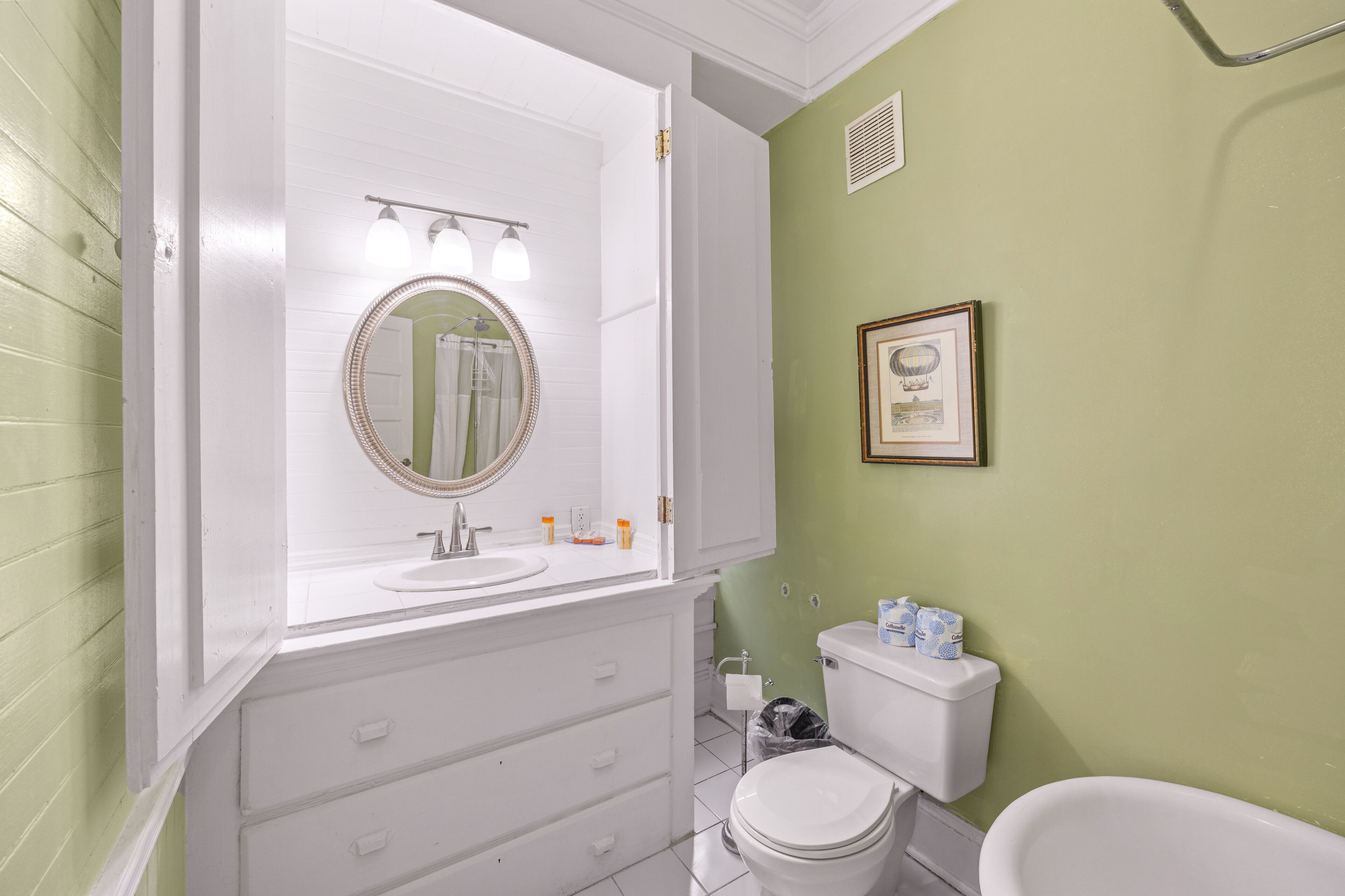 Een badkamer met een wit wastafelmeubel, een ronde spiegel, een toilet en een bad.