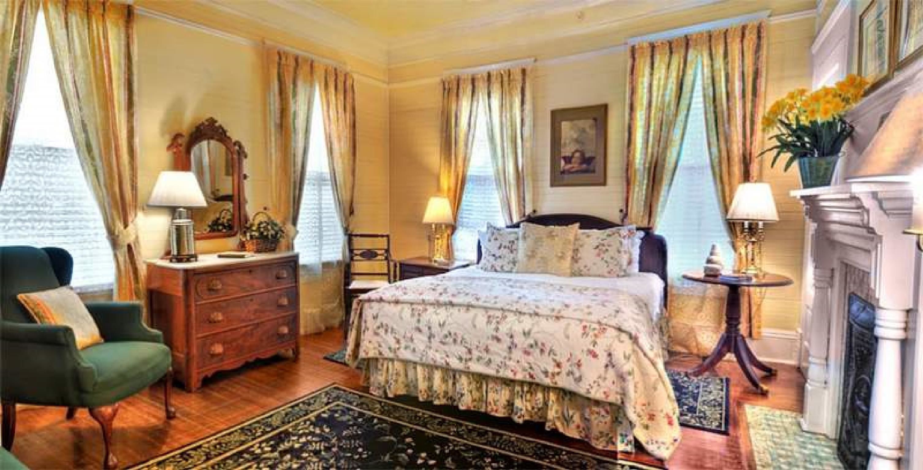 A classic hotel room with a bed, dresser, chair, and a fireplace.