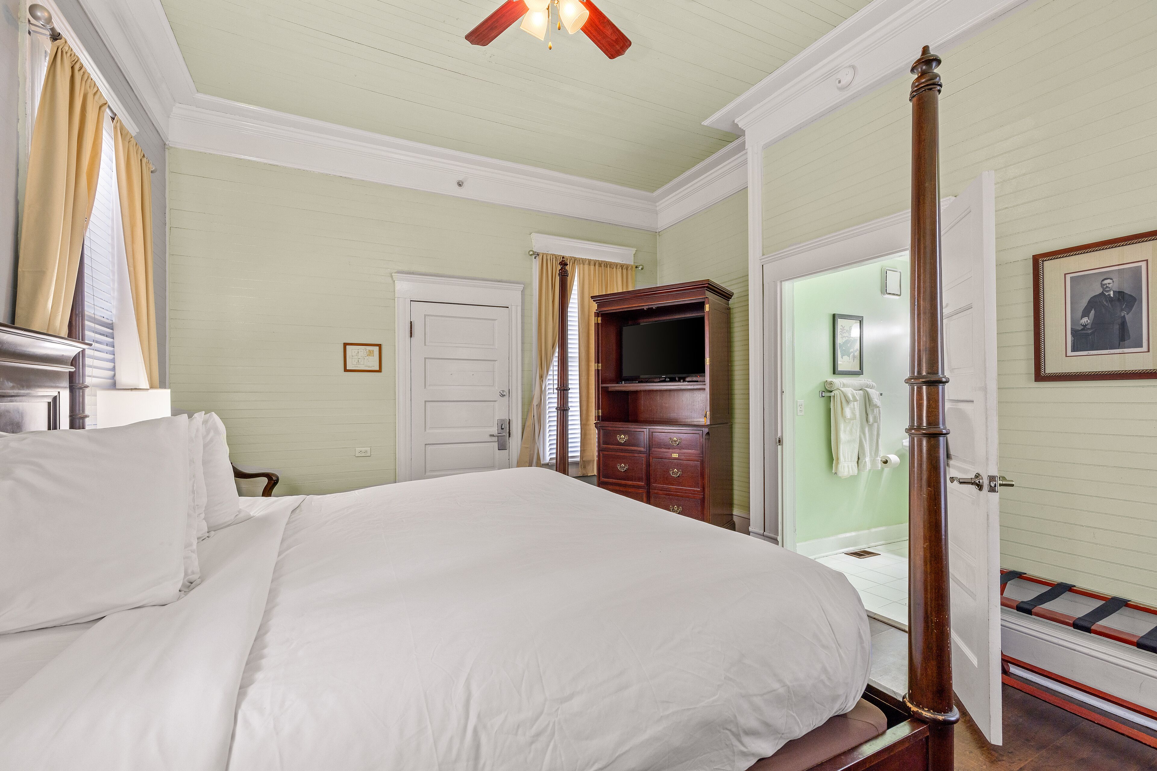 Une chambre avec un grand lit, une commode en bois, un téléviseur et une porte menant à la salle de bain.