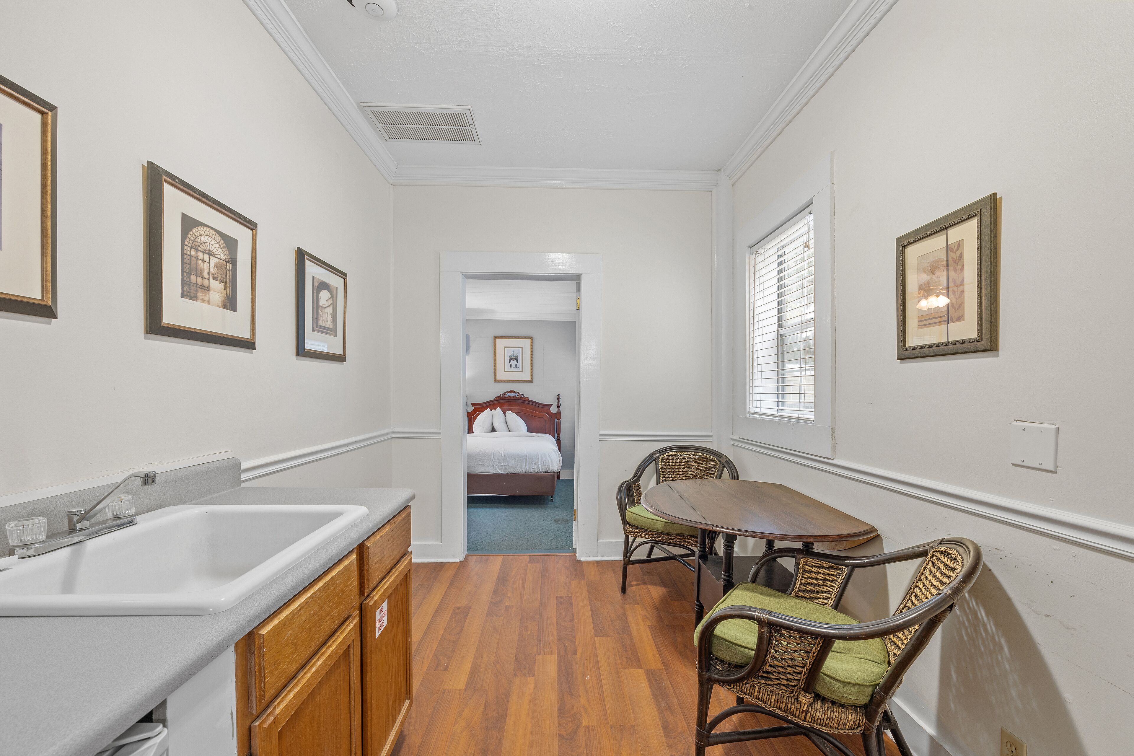 Une chambre d’hôtel équipée d’un coin cuisine, d’une table à manger avec des chaises, d’un lit et de tableaux encadrés aux murs.