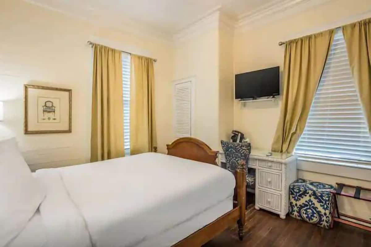 A hotel room with a bed, a desk, a chair, a television, and a window with curtains.