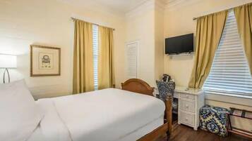 A hotel room with a bed, a desk, a chair, a television, and a window with curtains.