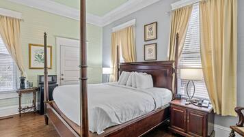 A four-poster bed in a room with a wooden floor, a white door, and a small table with a lamp.