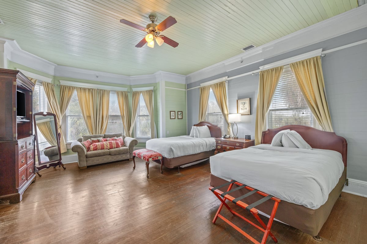 A room with a bed, a sofa, a wooden dresser, and a ceiling fan.