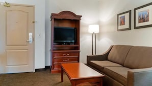 Une chambre d’hôtel avec un canapé, une télévision, une armoire en bois et une lampe.