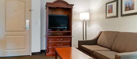 A hotel room with a sofa, a TV, a wooden cabinet, and a lamp.
