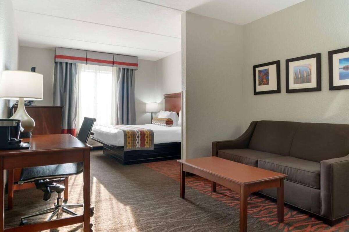 Una habitación de hotel con cama, escritorio, sofá y mesa de centro. Hay cortinas en la ventana y tres cuadros enmarcados en la pared.