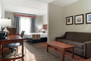 Una habitación de hotel con cama, escritorio, sofá y mesa de centro. Hay cortinas en la ventana y tres cuadros enmarcados en la pared.