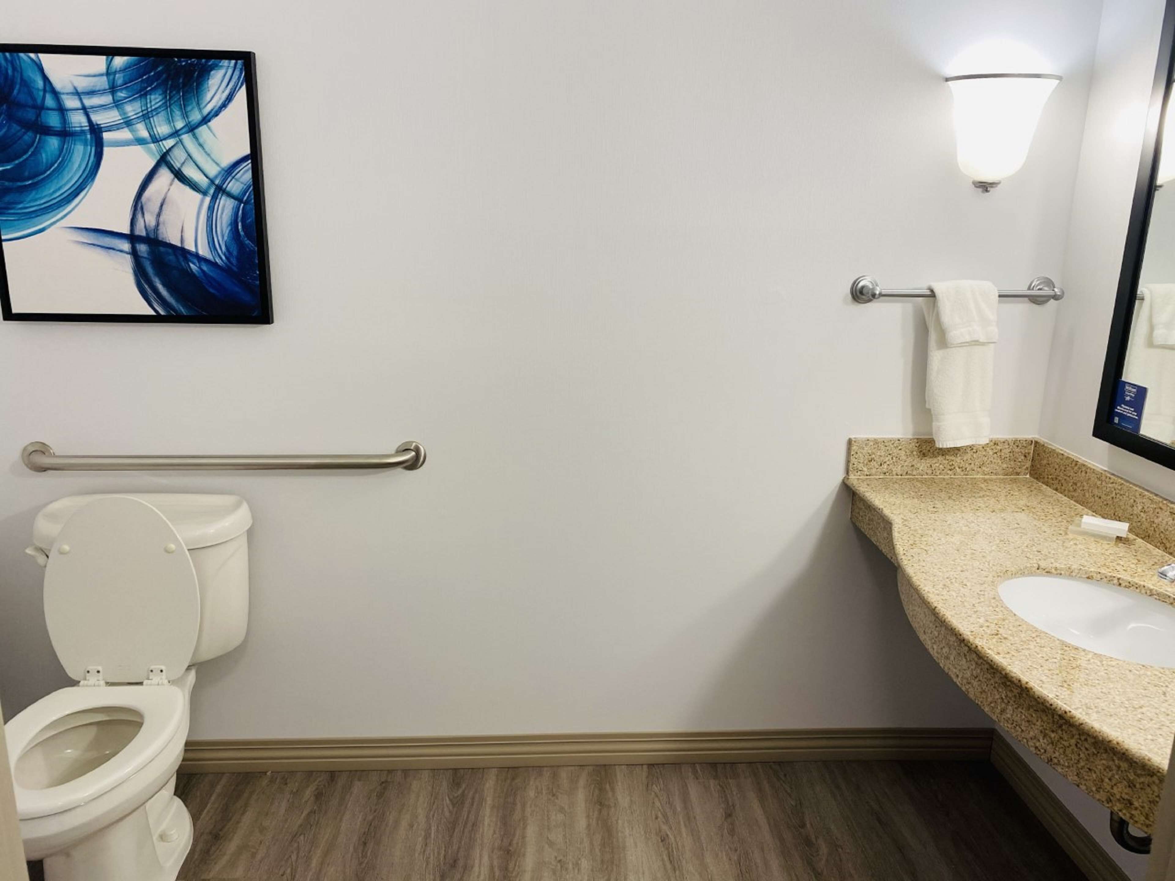 Un baño con inodoro, lavamanos, toallero y una lámpara en la pared.