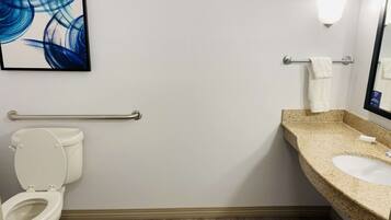 Un baño con inodoro, lavamanos, toallero y una lámpara en la pared.
