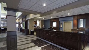 A hotel lobby with a reception desk, a trash can, and a patterned rug. - Hilton Garden Inn Des Moines West (West Des Moines)