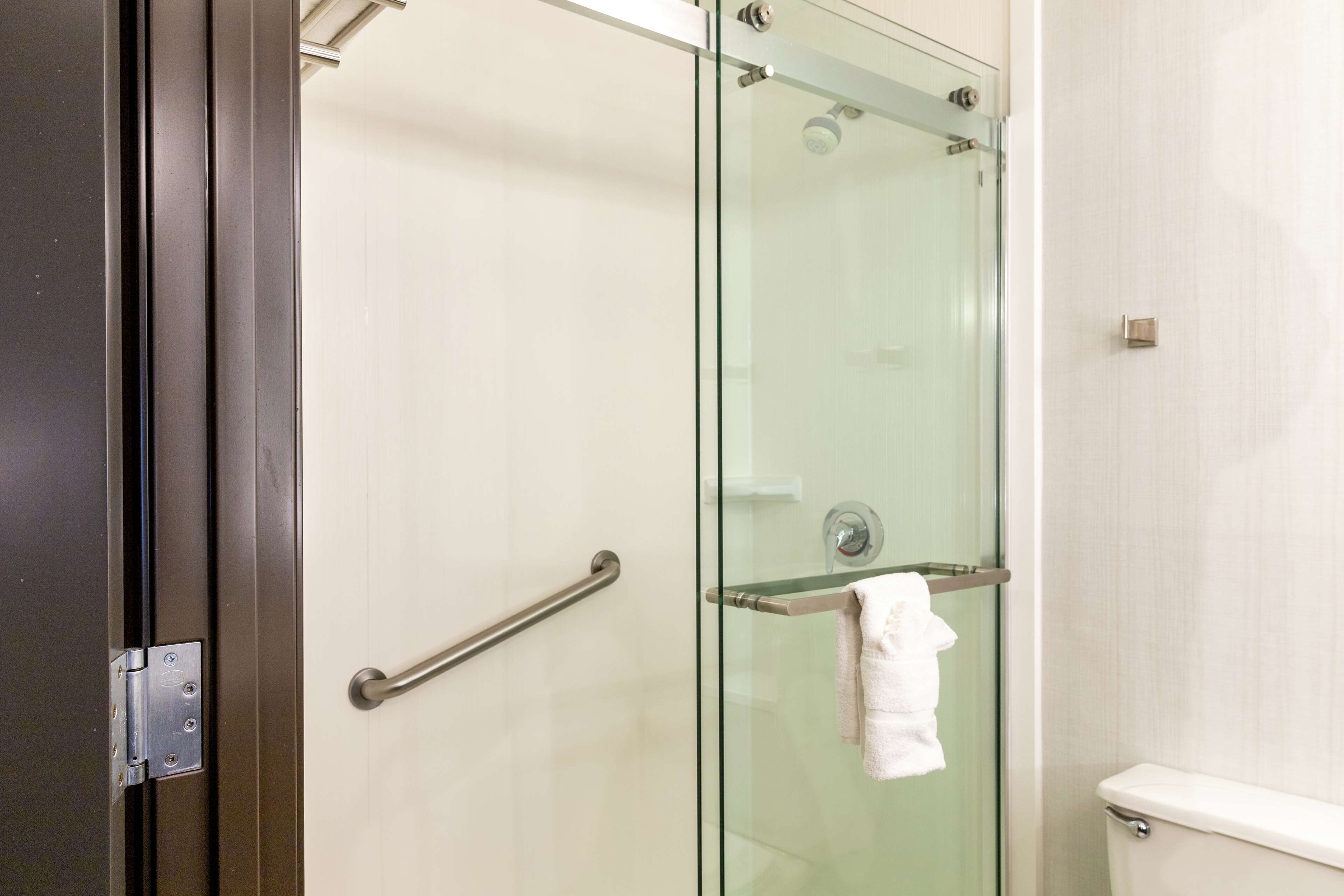 A glass-enclosed shower stall with a towel rack and a handrail.