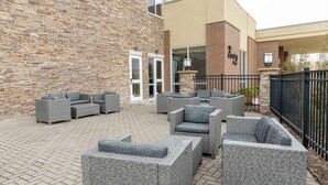 A patio area with wicker furniture and a brick wall. - Hilton Garden Inn Des Moines West (West Des Moines)