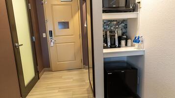 Un pasillo de hotel con una puerta, un microondas en un estante, una cafetera y un refrigerador.