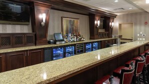 A bar area with a granite countertop, multiple refrigerators, and bar stools. - Hilton Garden Inn Des Moines West (West Des Moines)