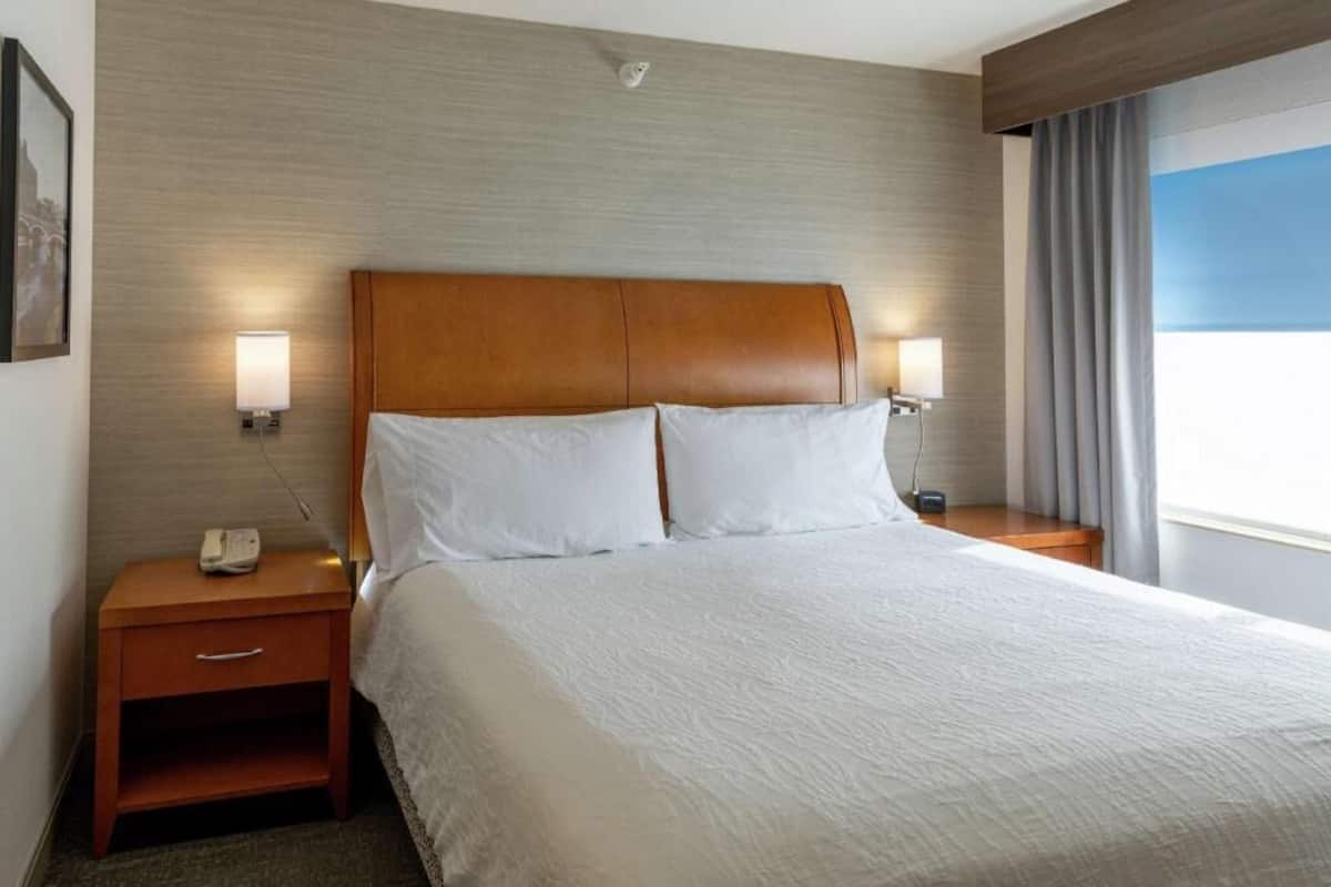 A hotel room with a large bed, two bedside lamps, a nightstand with a phone, and a window with curtains.