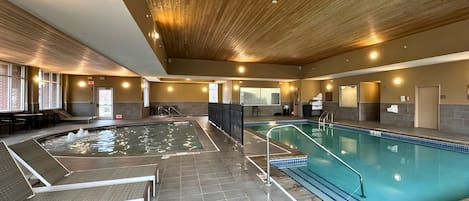 An indoor swimming pool with a wooden ceiling, tiled floor, and seating areas with loungers.