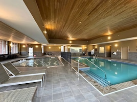 Una piscina interior con techo de madera, suelo de baldosas y zonas de estar con tumbonas.