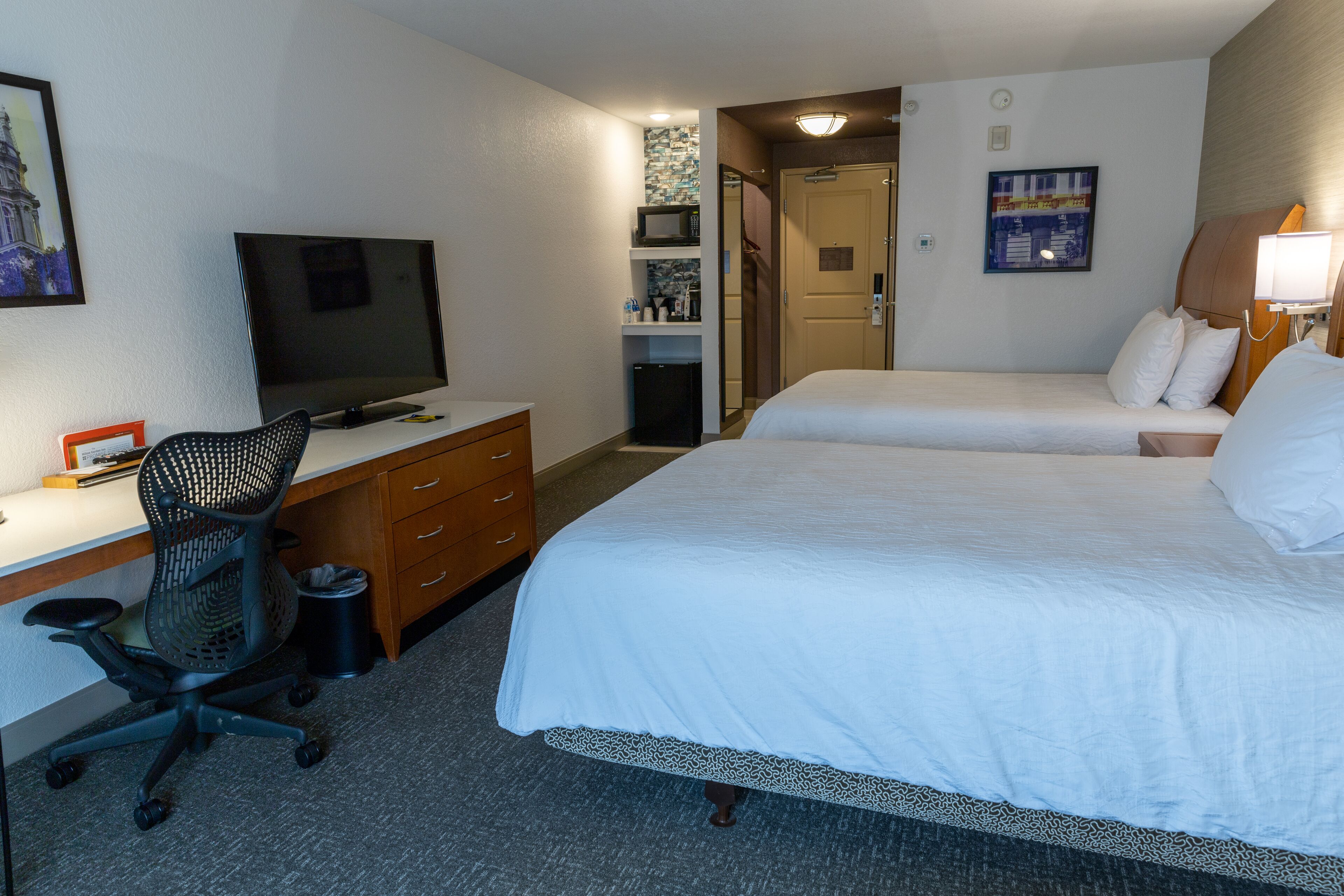 Une chambre d’hôtel comprenant un lit, un bureau avec un ordinateur, une chaise, une télévision et un petit réfrigérateur.
