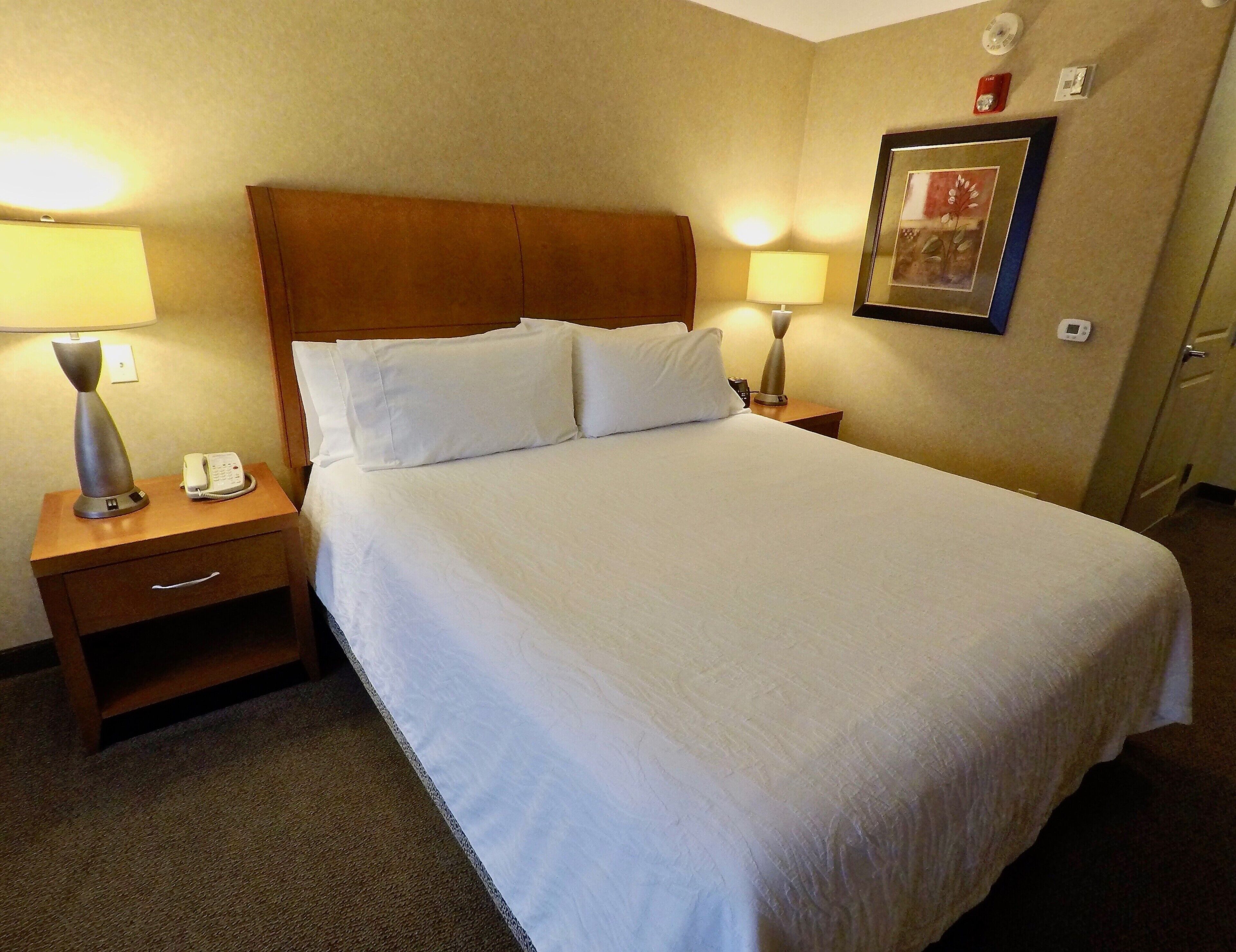 Une chambre d’hôtel avec un grand lit, deux tables de chevet avec des lampes, un téléphone et un tableau encadré au mur.