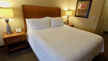 Une chambre d’hôtel avec un grand lit, deux tables de chevet avec des lampes, un téléphone et un tableau encadré au mur.