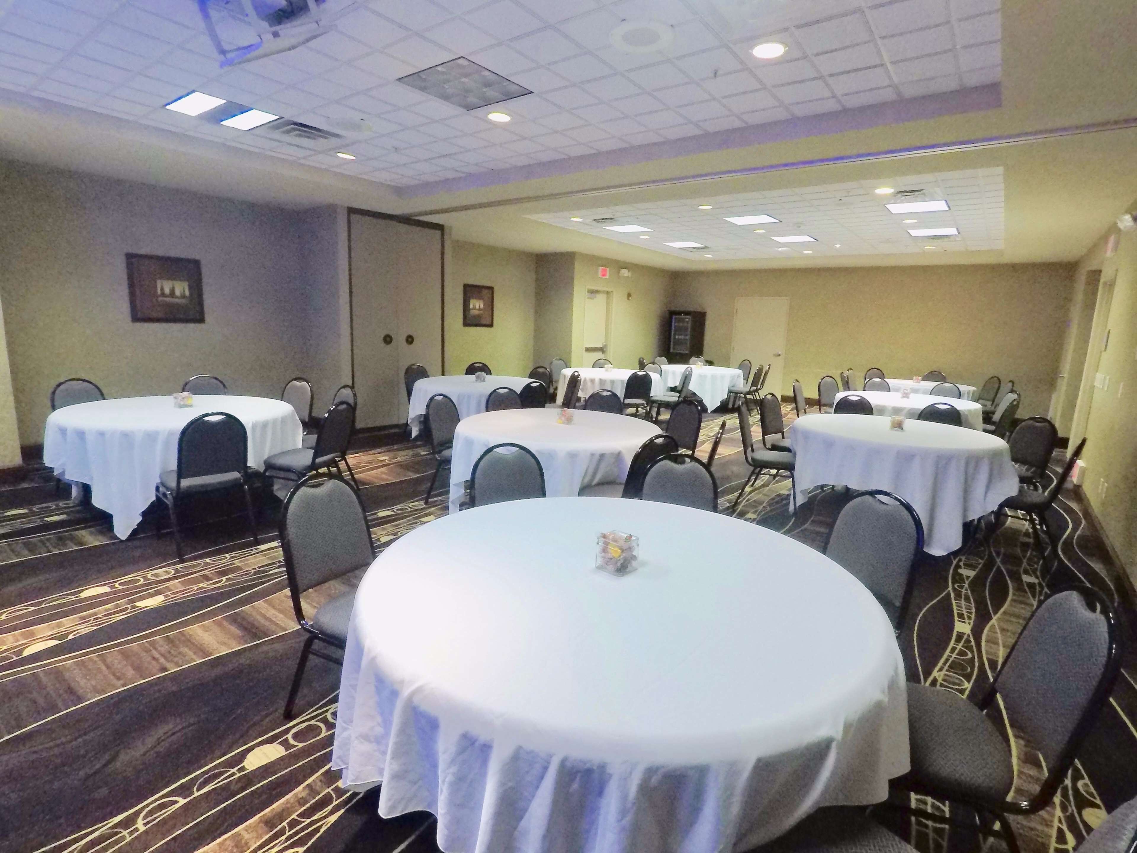 A conference room with multiple round tables, each surrounded by chairs, in a hotel setting.
