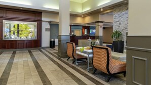 A hotel lobby with a reception desk, seating area, and a kitchen in the background. - Hilton Garden Inn Des Moines West (West Des Moines)