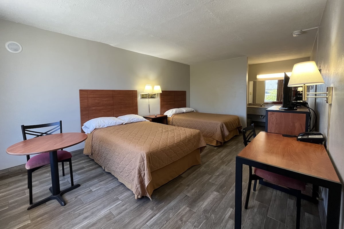 A hotel room with two beds, a desk, a chair, a table, and a TV.
