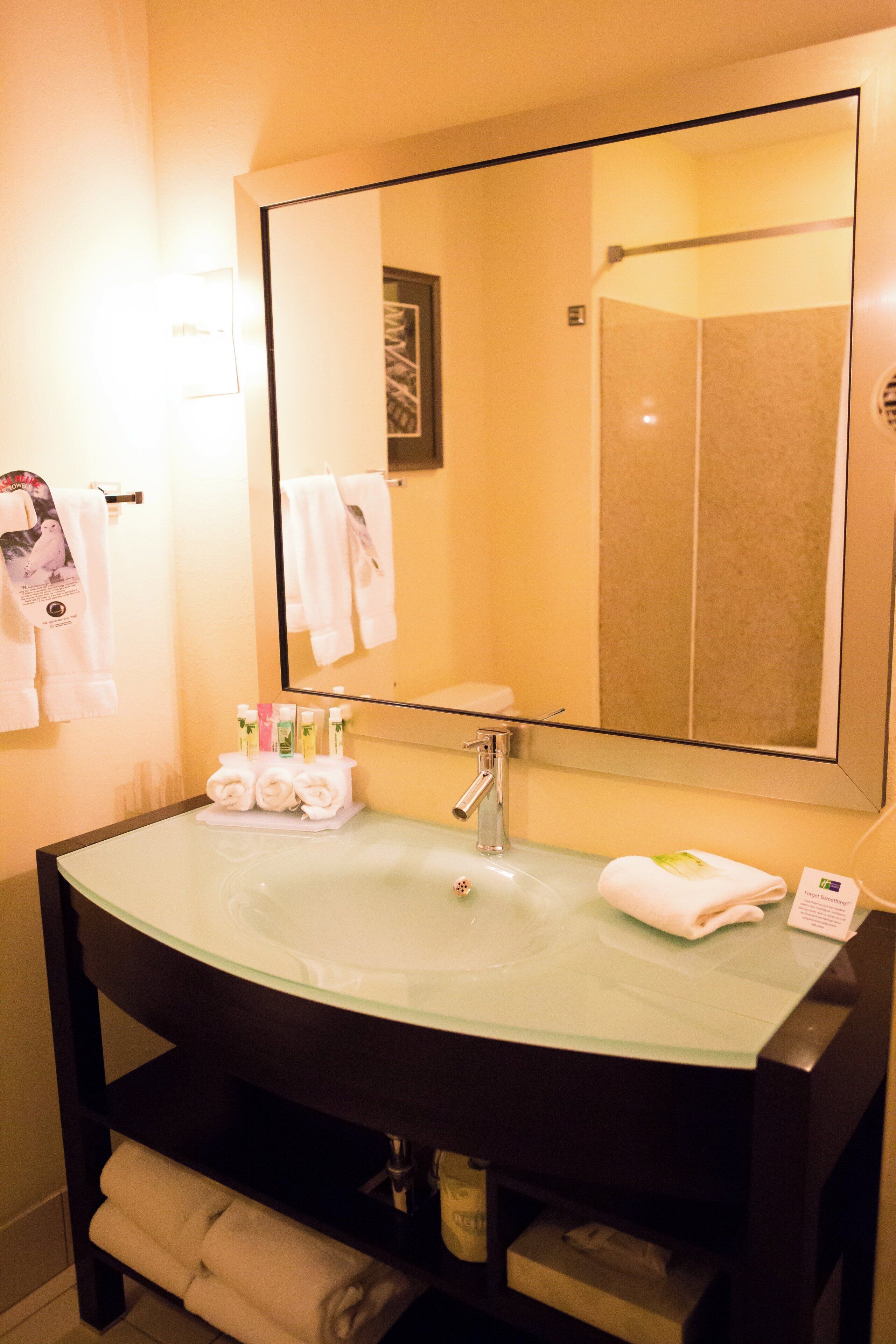 Une salle de bain d’hôtel avec un grand miroir, un lavabo et un porte-serviettes.
