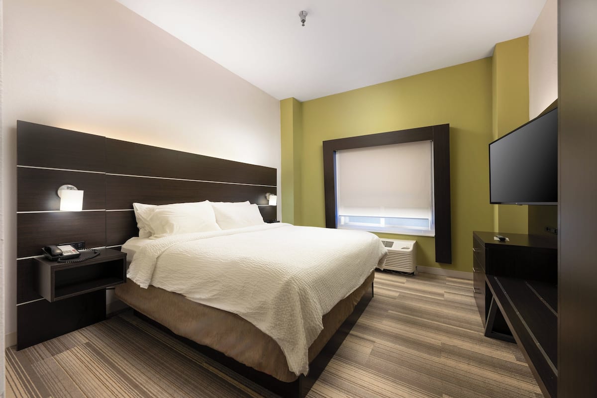 Ein Hotelzimmer mit einem großen Bett, Nachttischen, einem Fernseher und einem Fenster mit Jalousien.