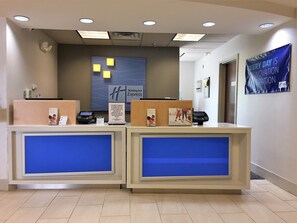 Ein Empfangsschalter eines Holiday Inn Express mit blauer Akzentwand, dem großen „H“-Logo und einem Banner mit der Aufschrift „Jeder Tag ist ein neuer Tag.“