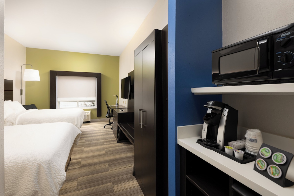 Une chambre d’hôtel avec deux lits, un bureau, un four à micro-ondes, une machine à café et une télévision.