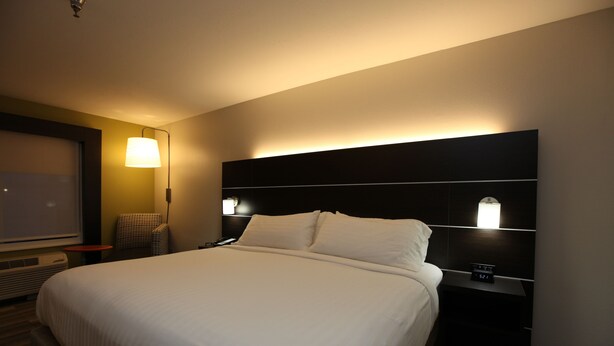 A hotel room with a large bed, a bedside table with a clock, a lamp, and a chair. - Holiday Inn Express Hotel & Suites Chattanooga-Hixson by IHG (Hixson)