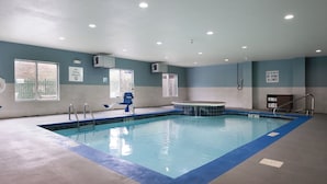 Una amplia piscina interior con agua azul cristalina, suelo con baldosas azules y blancas, y pared de color azul y blanco. Hay dos ventanas con marcos blancos y un cartel en la pared que dice “No se permite buceo”. 
