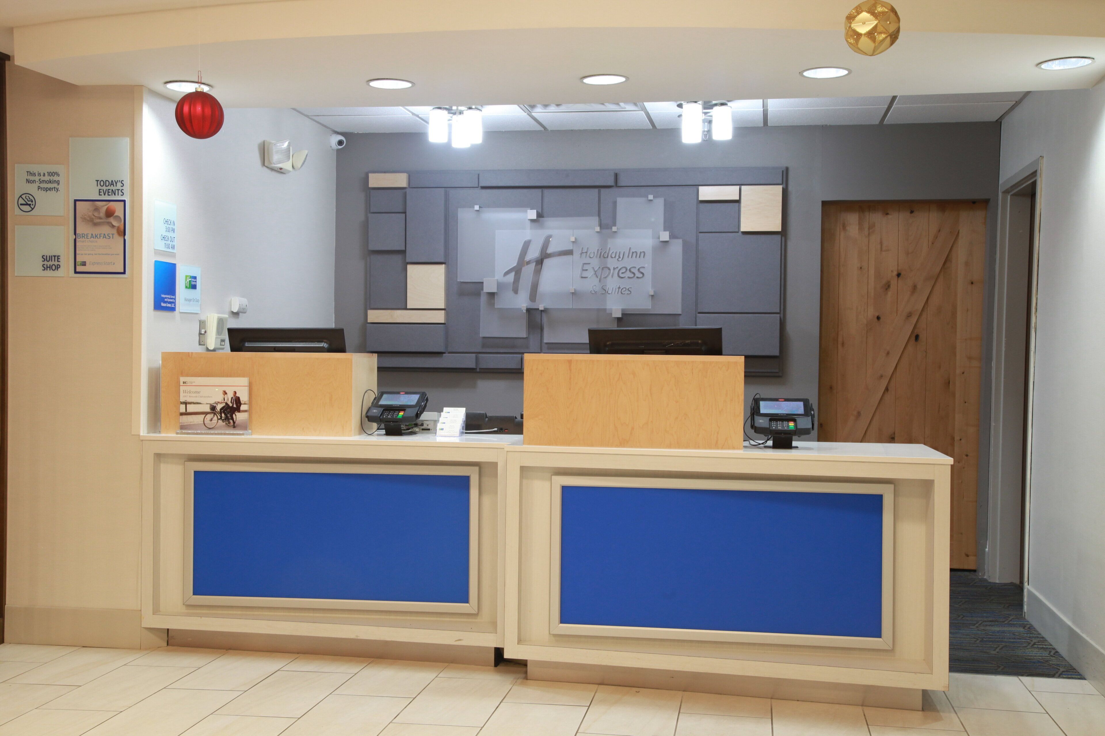 A hotel reception desk with two counters, a digital screen, and a sign indicating it's a non-smoking property.