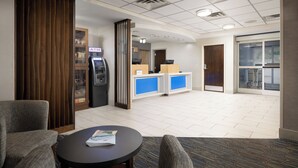 Un hall de hotel con una recepción, un cajero automático, un separador de madera y una zona de estar con una mesa y sillas.