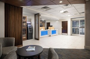 Un hall de hotel con una recepción, un cajero automático, un separador de madera y una zona de estar con una mesa y sillas.