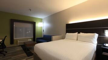 A hotel room with a large bed, a desk, a chair, a window, and a nightstand with a phone.
