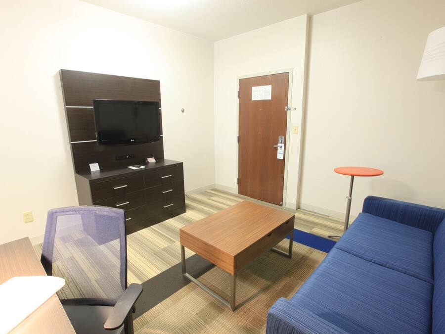 A hotel room with a television, a desk, a chair, a sofa, and a small table.