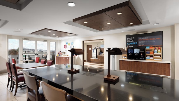 Un interior de cafetería moderna con una isla central, zona de estar y una exhibición de prensas de café.