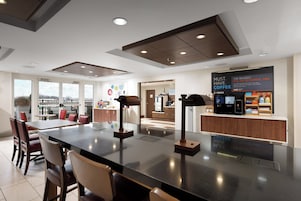 Un interior de cafetería moderna con una isla central, zona de estar y una exhibición de prensas de café.