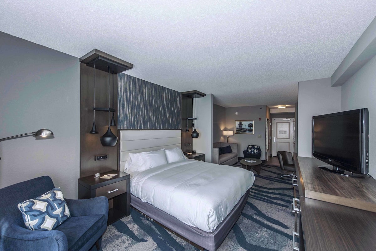 A hotel room with a bed, a desk, a television, a chair, and a desk lamp.