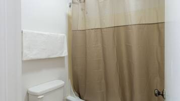 A bathroom with a toilet, a shower curtain, and a towel hanging on the wall.