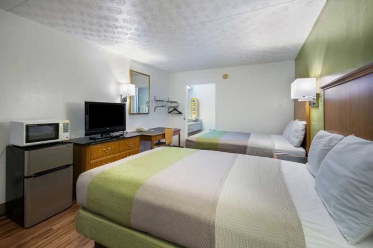 A hotel room with a bed, a desk with a computer, a television, and a refrigerator.
